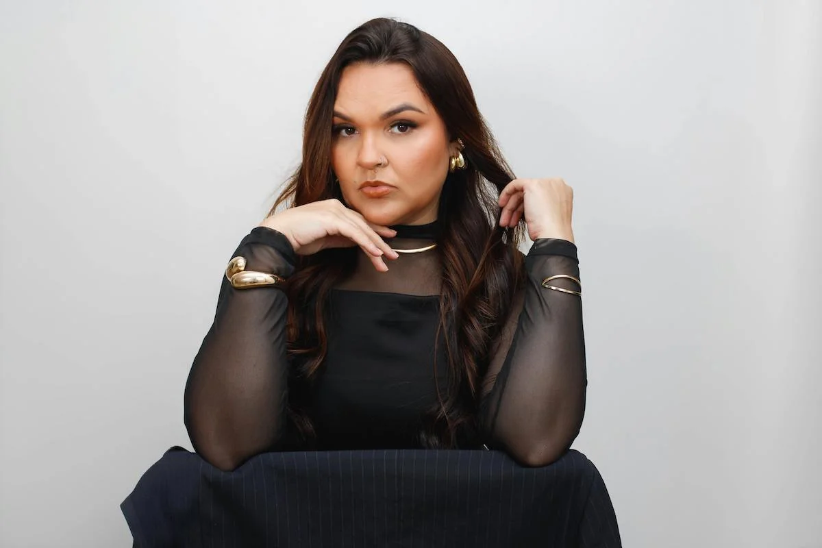 Une belle femme brune avec un top aux manches longues transparentes et des bijoux dorés