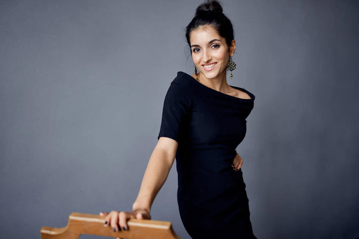 Une jolie femme brune et souriante avec un chignon dans une tenue de soirée sur fonds gris